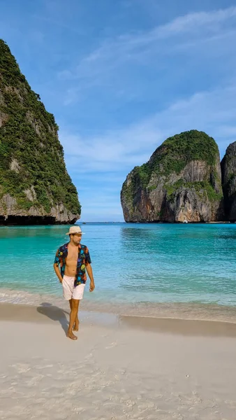 young white men with swim shorts and a hat on the beach of Maya Bay Koh Phi Phi Thailand.