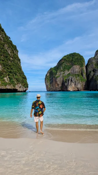 young white men with swim shorts and a hat on the beach of Maya Bay Koh Phi Phi Thailand.