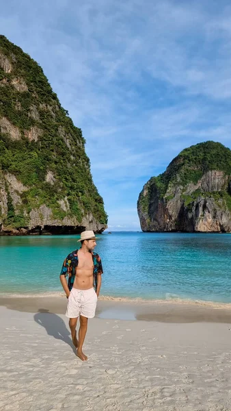 young sun tanning men with swim shorts and a hat on the beach of Maya Bay Koh Phi Phi Thailand.