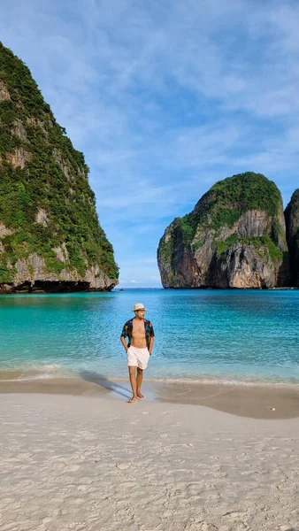 young caucasian men with swim shorts and a hat on the beach of Maya Bay Koh Phi Phi Thailand.