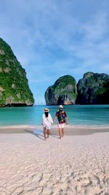 Birkaç beyaz adam ve Asyalı kadın sabahın köründe May Bay Koh Phi Phi Tayland sahilinde yürüyorlar.