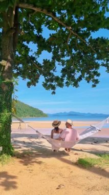 Erkekler ve kadınlar Koh Mak Tayland adasındaki bir hamakta. Tayland sahilinde Asyalı kadınlar ve beyaz erkekler.