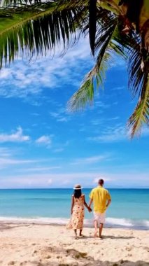 Koh Kood Tayland adasında tatilde olan bir çift kadın ve erkek palmiye ağaçlarıyla kumsalda yürüyorlar.