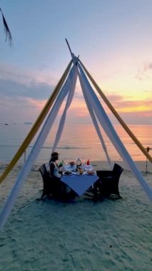 Gün batımında Asyalı Taylandlı kadınlar tatil sırasında Koh Chang Tayland sahilinde yemek yiyorlar..