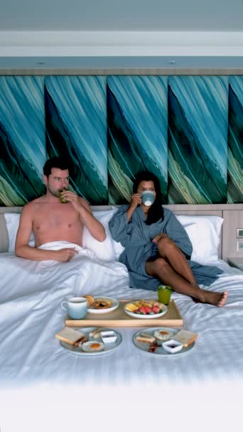 几个男人和女人在床上吃早餐 几个高加索男人和几个泰国女人在一家豪华酒店的卧室里吃早餐 — 图库视频影像
