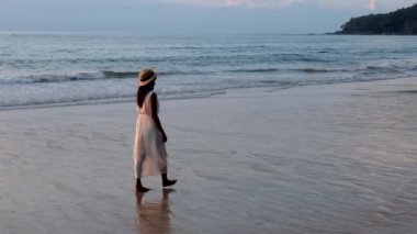 Khao Lak Tayland 'da günbatımında şapkalı Asyalı kadınlar sahilde yürürler.. 