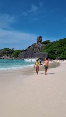Birkaç erkek kısa mayo ve kadınlar beyaz bir kumsalda ve turkuaz renkli okyanusta, denizde dev kayalar olan Similan Adaları Tayland 'da. 