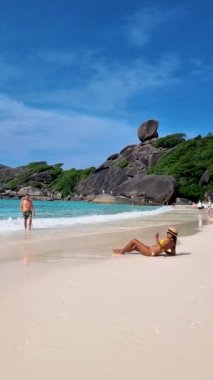 Similan Adaları Tayland 'da denizde dev kaya kütleleri olan beyaz bir kumsalda ve turkuaz renkli bir okyanusta yürüyen birkaç kadın ve erkek.. 