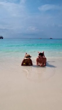 Similan Adaları Tayland 'da denizde dev kaya kütleleri olan beyaz bir kumsalda ve turkuaz renkli bir okyanusta oturan birkaç kadın ve erkek.. 