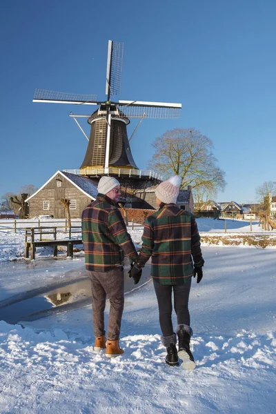 オランダの寒い冬の日に雪の中を歩く男女のカップル 雪の中で古い歴史的な木製の風車を背景に — ストック写真