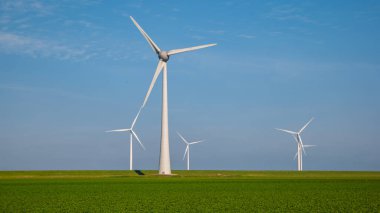 Yeşil tarlalı yel değirmeni türbinleri ve mavi gökyüzü yeşil enerji kavramı.