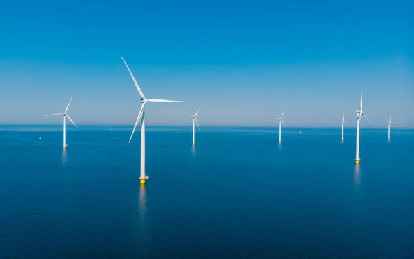 Windmill turbines at sea view from a drone aerial view from above at a huge windmill park with a blue ocean