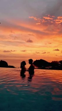 Sonsuz bir havuzda gün batımında okyanusa bakan bir çift kadın ve erkek..
