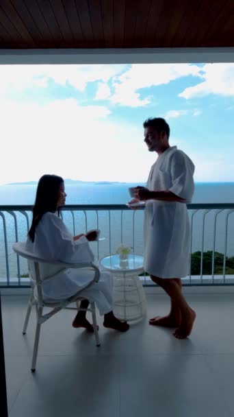 タイの海を眺めながらバルコニーでコーヒーを飲むアジア系の女性と白人男性のカップル — ストック動画