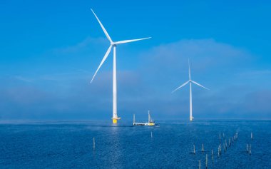 Balıkçı teknesi ve yel değirmeni türbinleriyle Windmill parkındaki hava manzarası, Hollanda Urk 'ta mavi gökyüzü yeşil enerji kavramına sahip elektrik üretiyor.