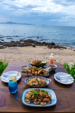 Gün batımında Pattaya Tayland sahilinde Tayland yemeği ve bbq balığı ile yemek masası.