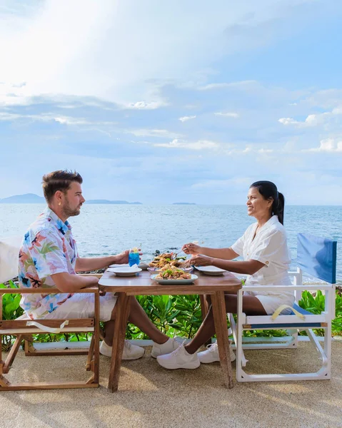 パタヤの海を眺めながらレストランで昼食をとるカップル日没時にパタヤの海沿いのレストランで夕食をとる男女 — ストック写真