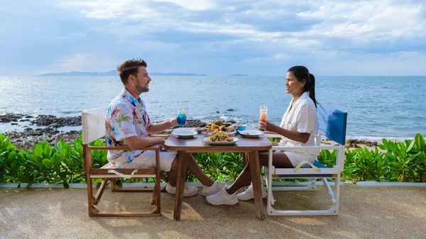 パタヤの海を眺めながらレストランで昼食をとるカップル日没時パタヤの海沿いのレストランで夕食をとる男女 — ストック写真