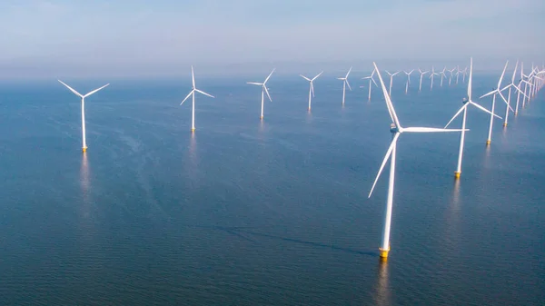 Windmill turbines at sea generating electric with a blue sky green energy concept. Drone aerial view at windmill park