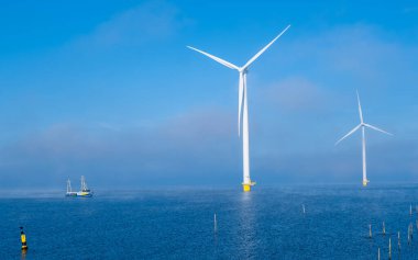 Rüzgâr değirmeni parkındaki hava manzarası kış boyunca yel değirmenleri türbinleriyle mavi gökyüzü yeşil enerji konseptiyle elektrik üretiyor. Bulutlu rüzgar değirmeni