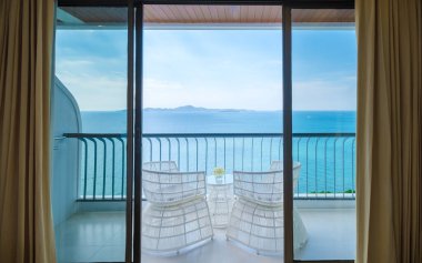 Bir otelin balkonunda mavi okyanus manzaralı sandalyeler.