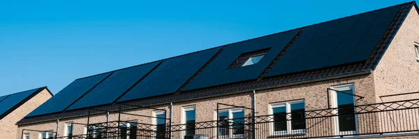 House with black solar panels attached to the roof against a sunny blue sky in the Netherlands. Sun energy from solar panels