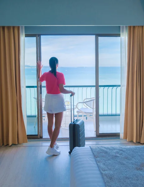 Thai women with hand luggage and a trolley checking in at a hotel room looking out over the ocean in Thailand.
