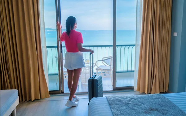 Thai women with hand luggage and a trolley checking in at a hotel room looking out over the ocean in Thailand.