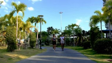 Pattaya Tayland 'da halka açık bir parkta koşan iki Asyalı kadın egzersizi. Palmiye ağaçlarıyla parkta koşan kız arkadaşlar.