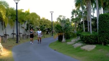 Pattaya Tayland 'da halka açık bir parkta koşan iki Asyalı kadın egzersizi. Gün batımında yeşil bir parkta koşan kız arkadaşlar