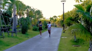 Pattaya Tayland 'da halka açık bir parkta koşan iki Asyalı kadın. Kadın arkadaşlar palmiye ağaçlarıyla yeşil bir parkta koşuyorlar.