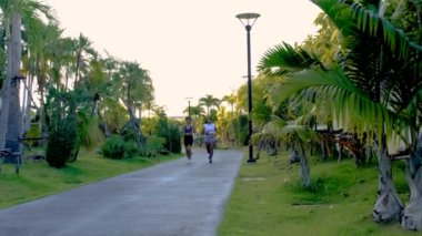 Pattaya Tayland 'da halka açık bir parkta koşan iki Asyalı kadın. Kadın arkadaşlar palmiye ağaçlarıyla yeşil bir parkta koşuyorlar.
