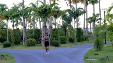 Pattaya Tayland 'da bir halk parkında koşan Asyalı kadınlar. Palmiye ağaçlarıyla yeşil bir parkta koşan kadın egzersizi.