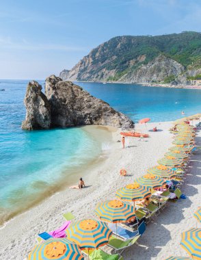 Çakıl taşı plajı Monterosso tatili Cinque Terre Monterosso al Mare sandalyeleri ve şemsiyeler yaz boyunca Cinque Terre İtalya 'nın bir parçası olan Spiaggia di Fegina plajını dolduruyor.