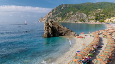 Çakıl taşı plajı Monterosso tatili Cinque Terre Monterosso al Mare Sandalyeleri ve şemsiyeler güneşli bir günde Cinque Terre İtalya 'nın bir parçası olan Spiaggia di Fegina plajını dolduruyor.