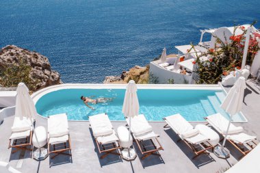 Santorini Yunanistan Oia, havuzda dinlenen yüzme şortlu gençler Yunanistan Santorini Adası kalderasına, sonsuz havuza, Avrupa 'da lüks bir tatile çıkan genç bir adam Yunanistan' a bakıyorlar.