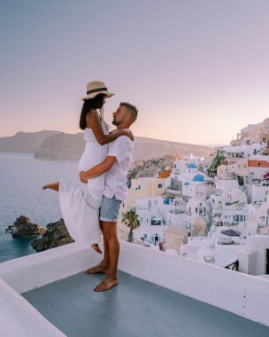 Santorini Yunanistan, Santorini Adası 'nda tatil yapan genç bir çift mavi kubbe kilisesi ve beyazlatılmış Oia Santorini köyü, Asyalı kadınlar ve beyaz tenli erkekler tarafından gün doğumunu izliyor. 