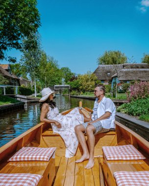 Çift Giethoorn Hollandalı çifti, Avrupa 'da sıcak bir bahar gününde bir çiftlikte, kanalı ve sazdan çatı evlerini gören ünlü köy manzaralı bir tekneyle köyü ziyaret ediyor.