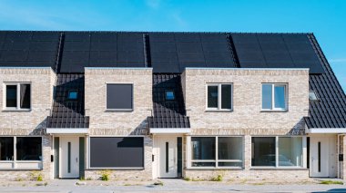 Çatıya güneş panelleri takılı yeni evler güneşli bir gökyüzüne karşı, siyah güneş panelleri olan yeni binalar. Zonnepanelen, Zonne Energie, Çevirisi: Güneş enerjisi. Hollanda