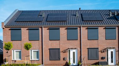 Çatıya güneş panelleri takılı yeni evler güneşli bir gökyüzüne karşı, siyah güneş panelleri olan yeni binalar. Zonnepanelen, Zonne Energie, Çevirisi: Güneş enerjisi. Hollanda