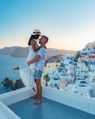 Santorini Yunanistan, Santorini Adası 'nda tatil yapan genç bir çift mavi kubbe kilisesi ve beyazlatılmış Oia Santorini köyü, Asyalı kadınlar ve beyaz tenli erkekler tarafından gün doğumunu izliyor. 