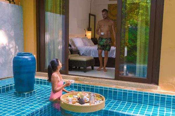 A couple having breakfast in the swimming pool, Asian women and Caucasian men having floating breakfast in the pool during vacation