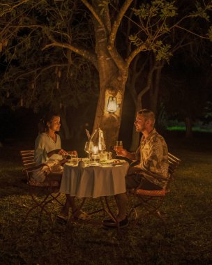 couple men and woman romantic dinner on a luxury safari, South Africa l, a luxury safari lodge in the bush of a Game reserve clipart
