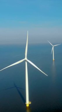 Denizdeki rüzgar türbinlerinin insansız hava aracı görüntüsü, bulutlu ve mavi gökyüzü olan yel değirmeni parkı, okyanus havası manzaralı rüzgar türbini Flevoland Hollanda 'daki Ijsselmeer.