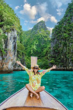 Kho Phi Phi Tayland 'da uzun kuyruklu bir teknenin önünde ellerini kaldıran Asyalı kadınlar, Pileh Lagoon' da bir teknenin önünde duran kadınlar.