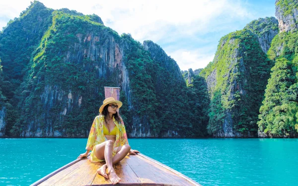 Asian women in front of a longtail boat at Kho Phi Phi Thailand, women in front of a boat at Pileh Lagoon with turqouse colored ocean