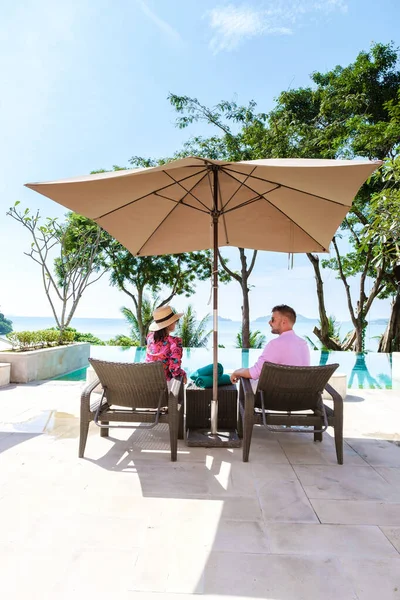 一对中年男人和一个女人在一个豪华的海滩椅子上 在泰国的一个豪华假期里 男人和一个亚洲女人在游泳池外观看日落 海洋上无边的游泳池 — 图库照片