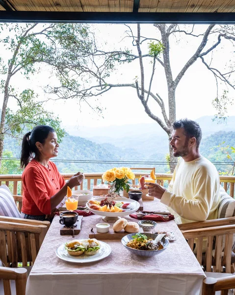 A Couple have breakfast outdoor, luxury breakfast in the mountains of Chiang Mai Thailand, luxury breakfast with Chiang Mai curry noodle soup or Khao Soi Gai and fruits and coffee on the table.
