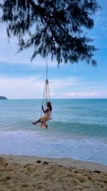 Couple of men and women at a swing on the beach of Koh Kood Island in Thailand.