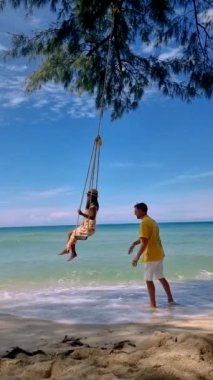 Couple of men and women at a swing on the beach of Koh Kood Island in Thailand.